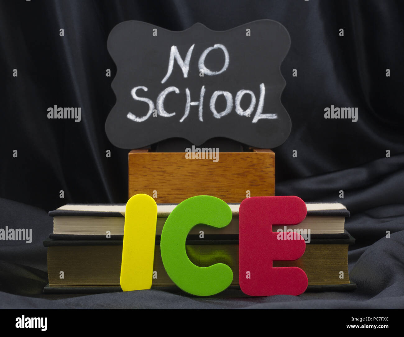 ICE in letters with NO SCHOOL on small chalkboard with books and black satin background. Icy weather conditions create danger and school closings. Stock Photo