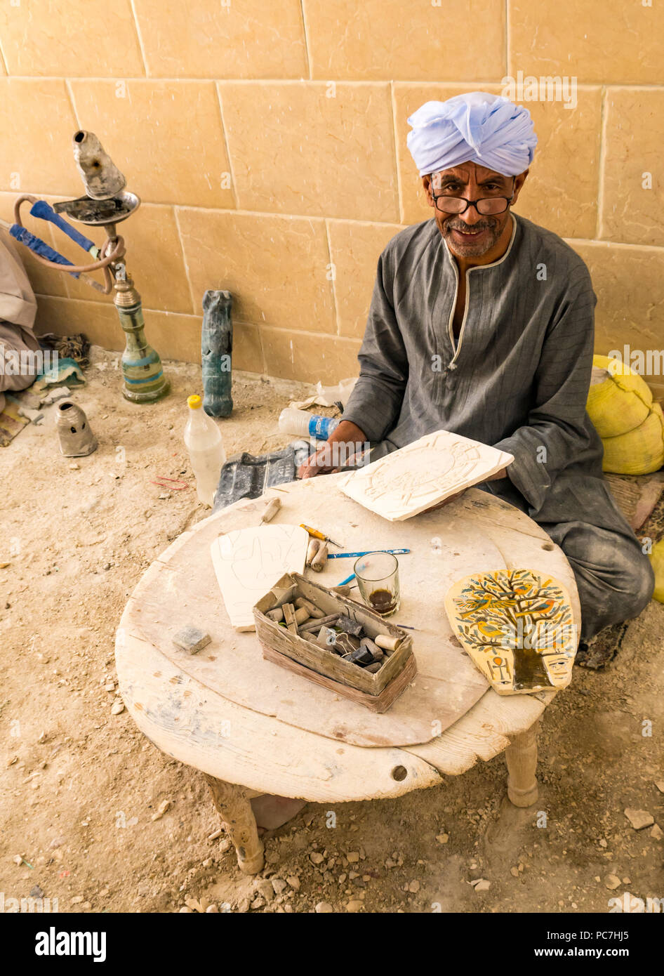 Old Egyptian man in robe and turban painting Tree of Life art for sale at tourist shop, West Bank, Luxor, Egypt, Africa Stock Photo