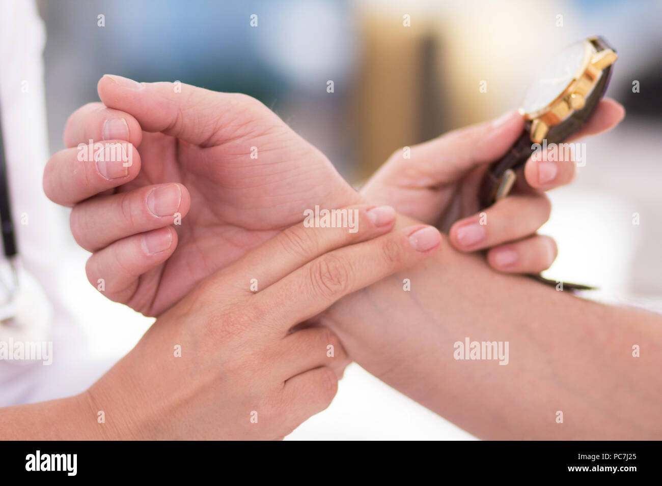 Female doctor checking patients pulse using wrist watch. Close up shot of female hand holding two fingers to another persons wrist for checking pulse. Stock Photo
