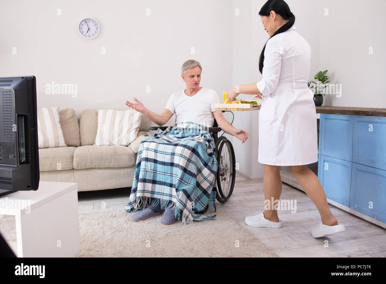 Caregiver bringing food to aged man. Pretty female doctor walking into living room with food on