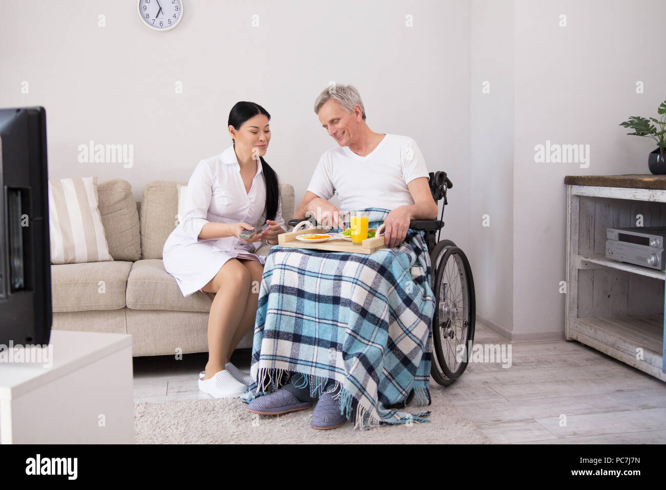 Elderly man eating in wheelchair with his caretaker sitting next to him
