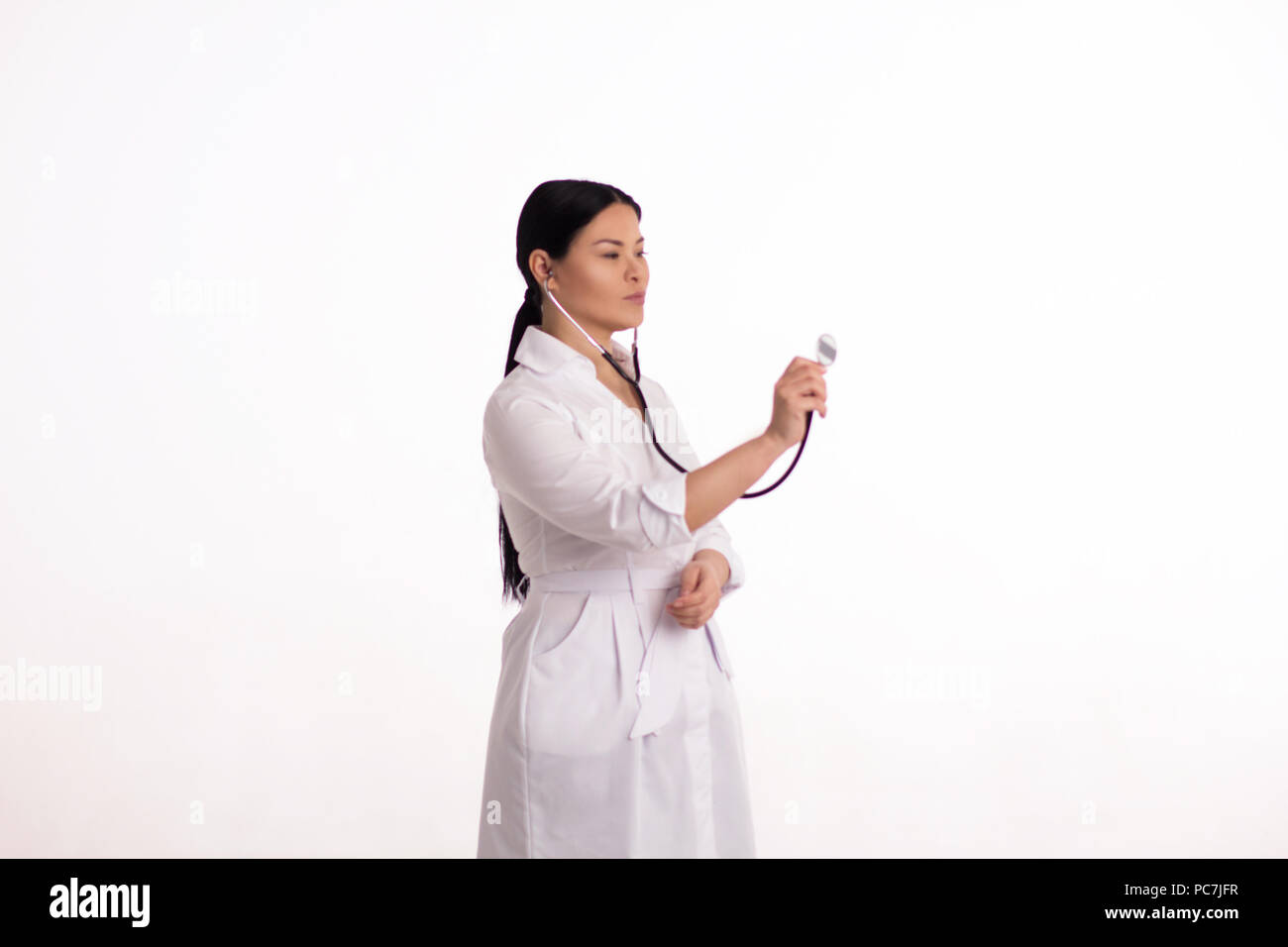 Young gorgeous nurse using stethoscope in air. Studio portrait of asian ...