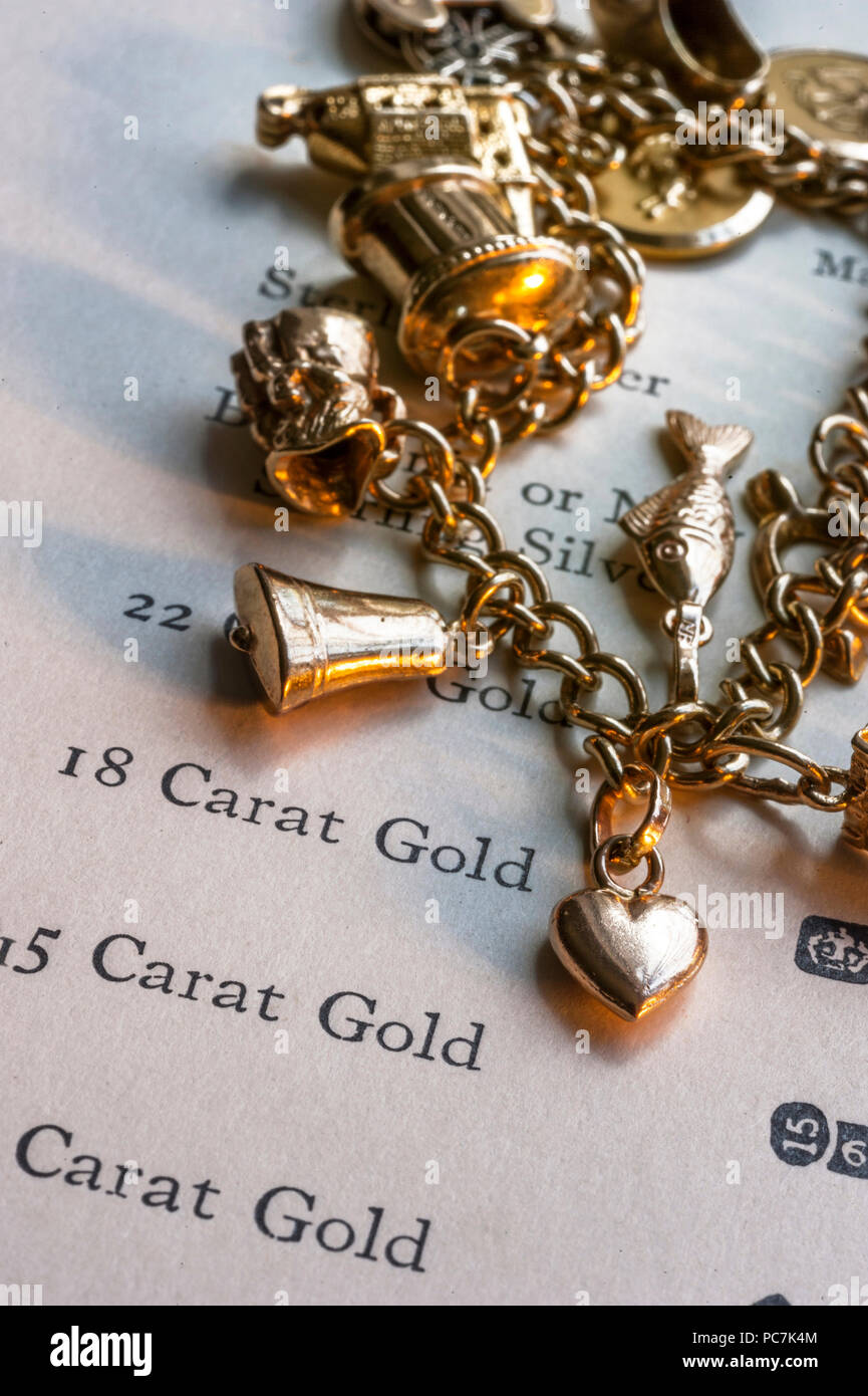 GOLD CHARMS SCRAP ANTIQUE GOLD CARAT PURITY HEART 1960's gold charm bracelet & page of gold purity hallmarks reference book for scrap value evaluation Stock Photo