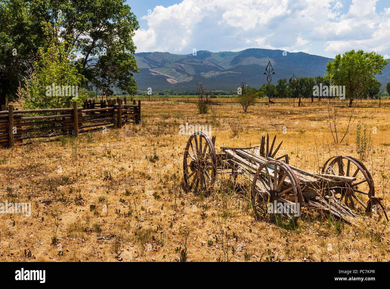 TAOS, NM, USA-8 JULY  18: An ancient, deteriorating wagon with wood spokes and metal rims sits abandoned in a field beside Overland Sheepskin Ranch. Stock Photo