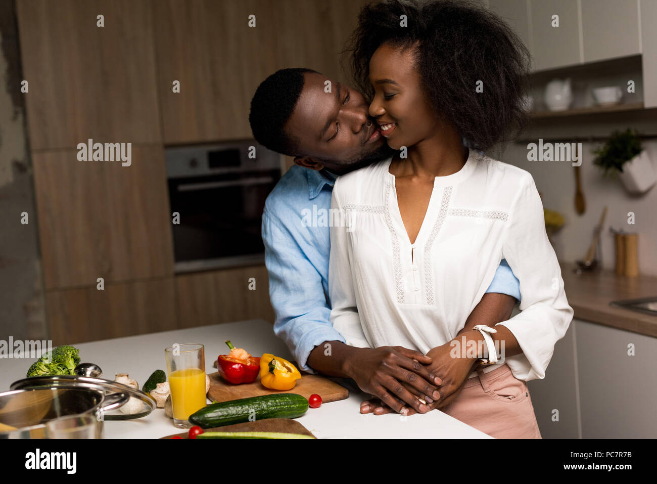 Smiling african american couple hugging near table with vegetables and ...