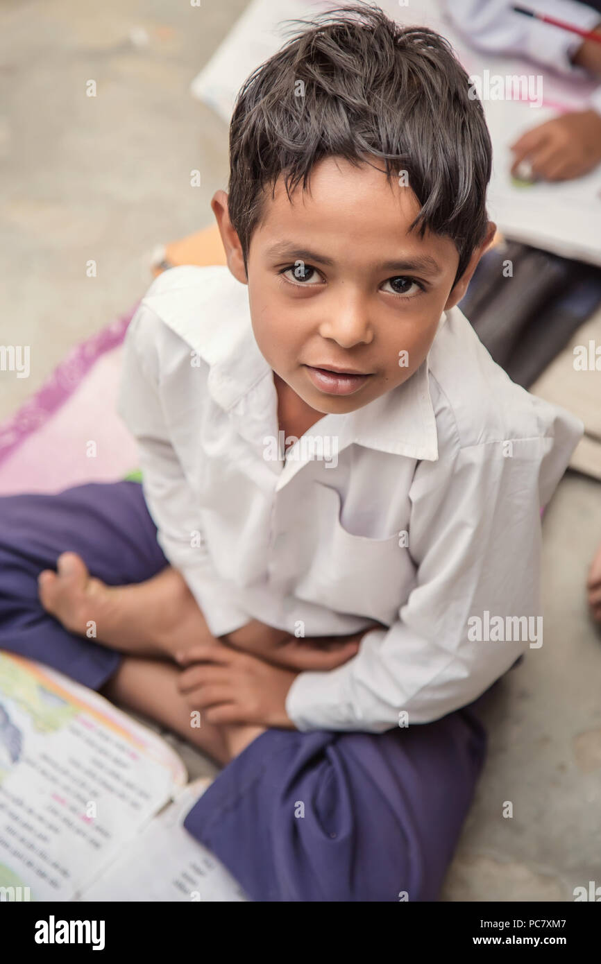 School boy sitting on the floor of primary school in uniform having his note book in front of him.  Selective focus, shallow depth of field. Stock Photo