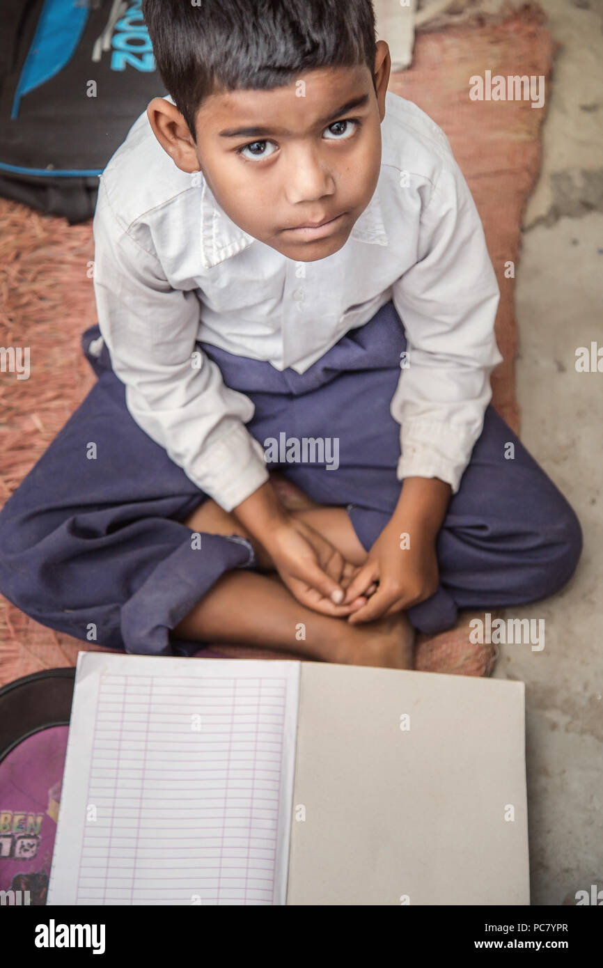 School boy sitting on the floor of primary school in uniform having his note book in front of him. Selective focus, shallow depth of field. Stock Photo
