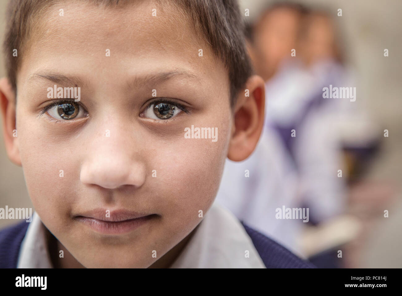 Boy sitting on the floor of government primary school in uniform along with some of his class mates sitting behind. Selective focus, shallow depth of  Stock Photo