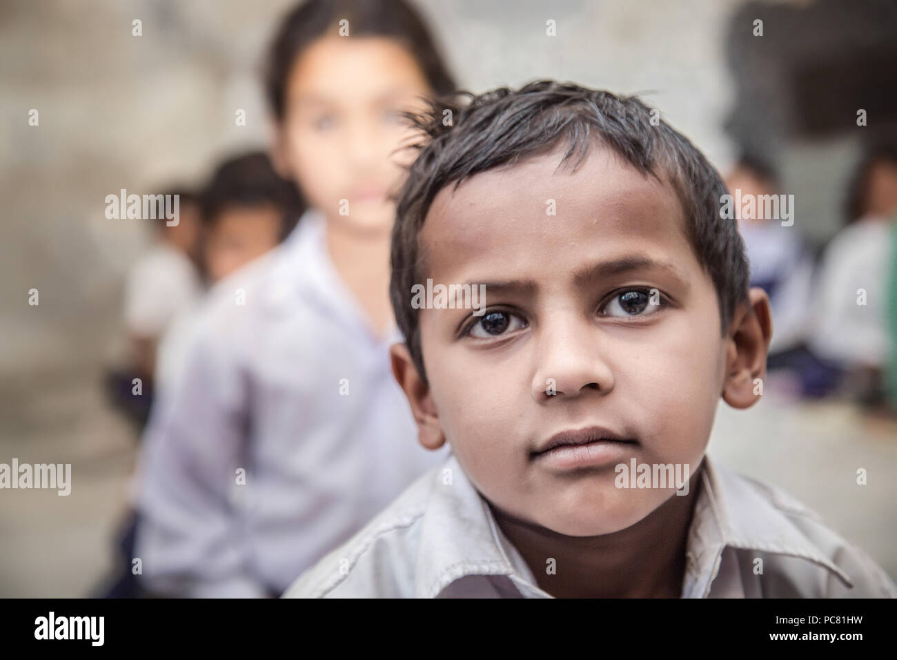 Boy sitting on the floor of government primary school in uniform along with some of his class mates sitting behind. Selective focus, shallow depth of  Stock Photo