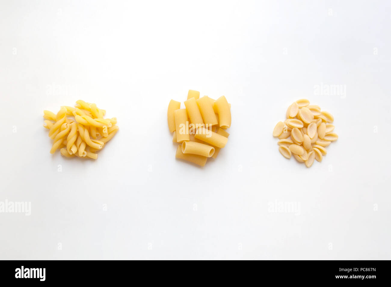 Three heaps of raw wheat pasta with various shapes isolated on white background Stock Photo