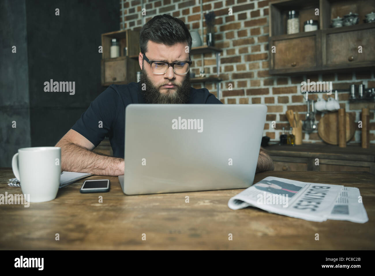 Focused bearded young man using laptop and working at wooden table Stock Photo