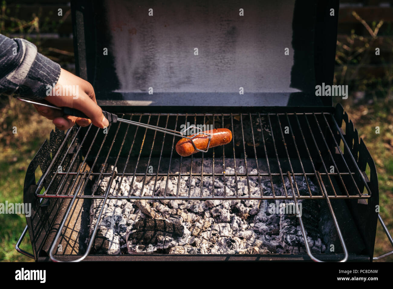 Man with serving tongs cooking sausages outdoors on grill Stock ...