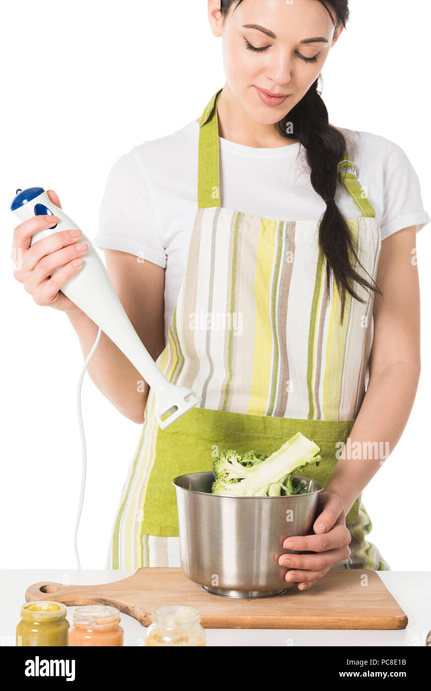 young woman with hand blender in hand at table with broccoli in saucepan Stock Photo