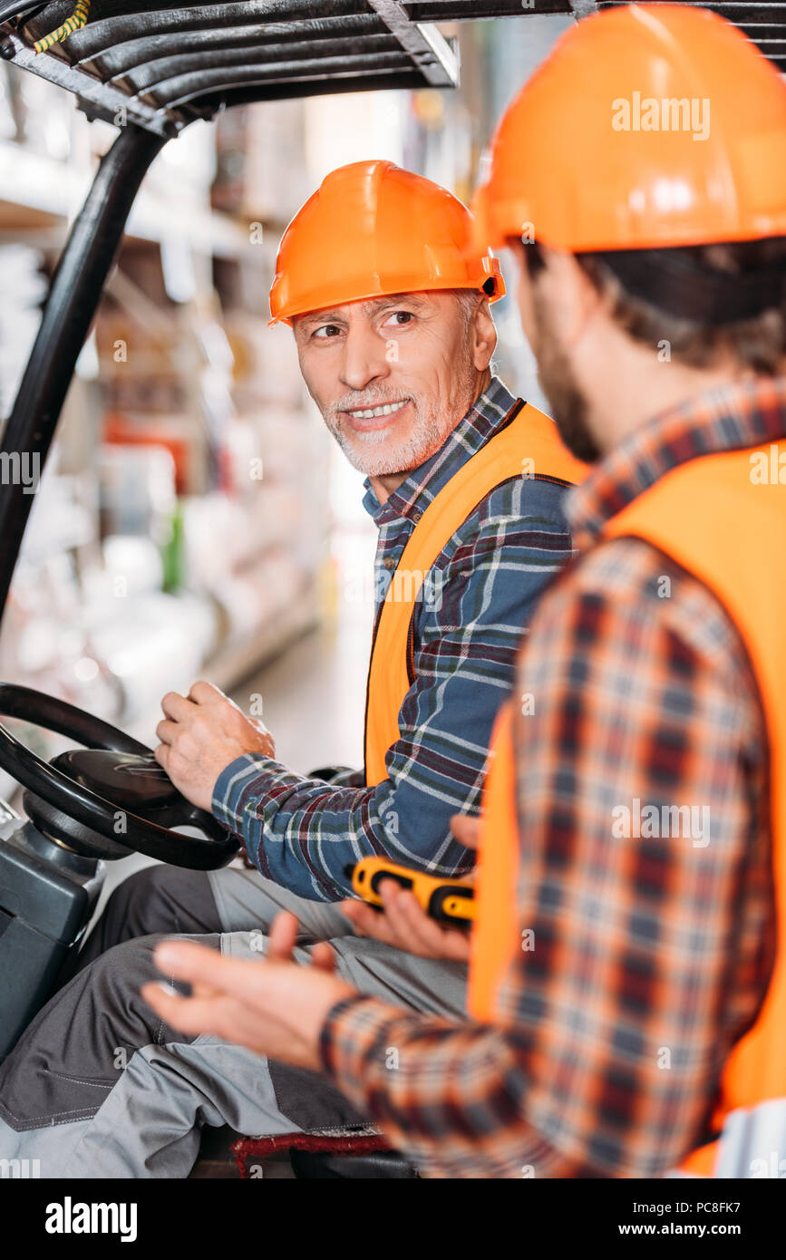 senior worker in safety vest and helmet sitting in forklift machine and