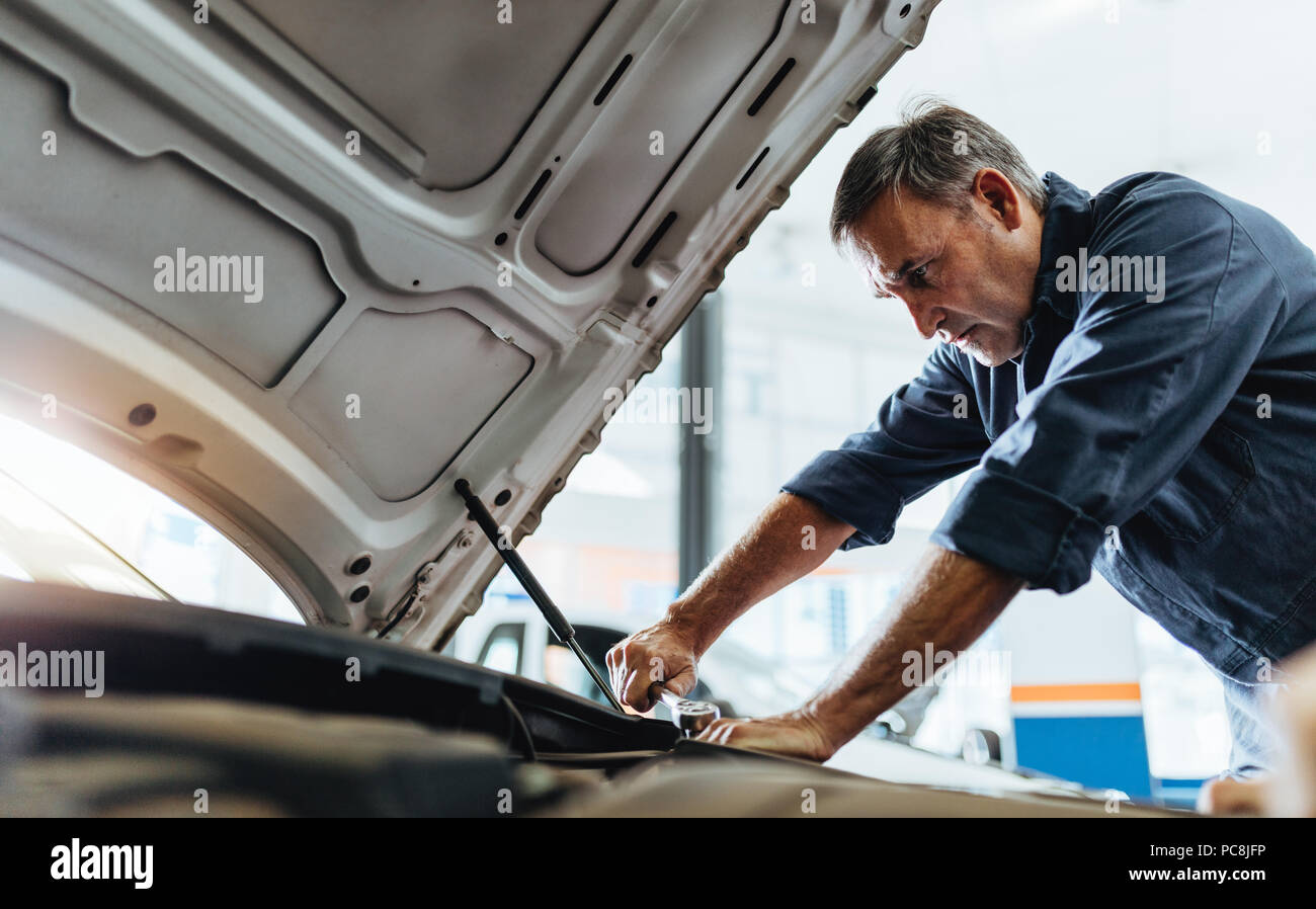 Male mechanic repairing the car in auto service center. Mechanic in uniform fixing a vehicle. Stock Photo
