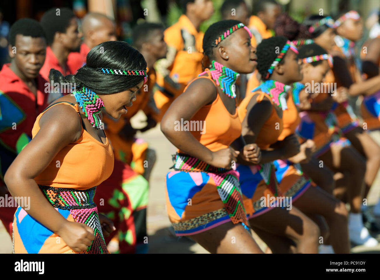 Young women and men of street performer group performing traditional Zulu songs in colourful dress at uShaka Marine World, Durban Stock Photo