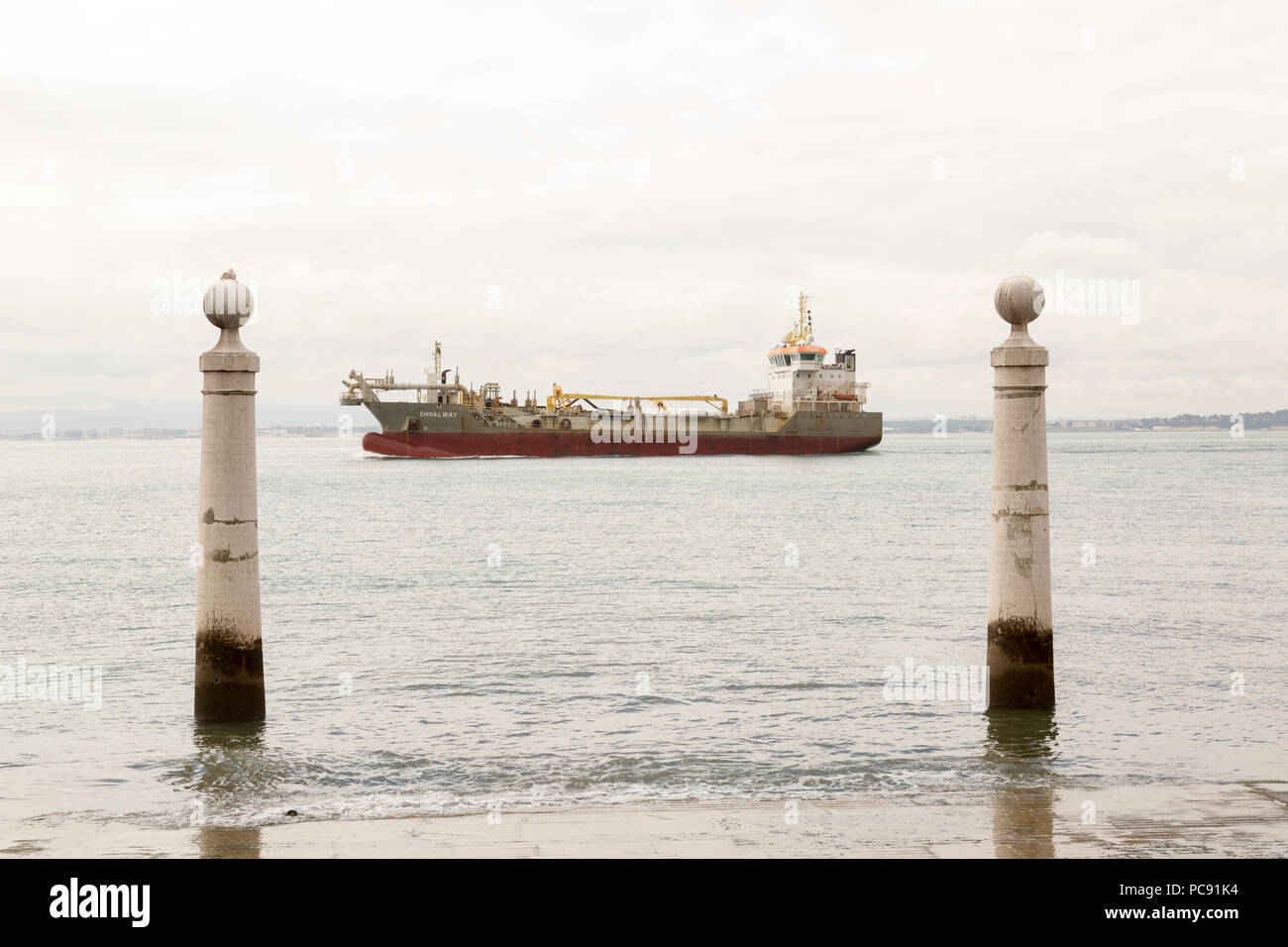 A couple of Pombaline pillars defining lisbon's gateway to the sea, on the Tagus River with a freighter centered between the two in Portugal. Stock Photo