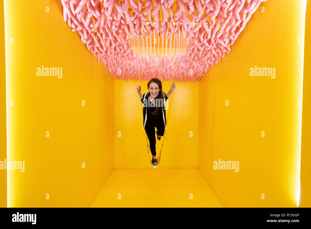 A woman stands on a swing in a multicolored room at the Museum of Ice Cream in San Francisco, California. Stock Photo