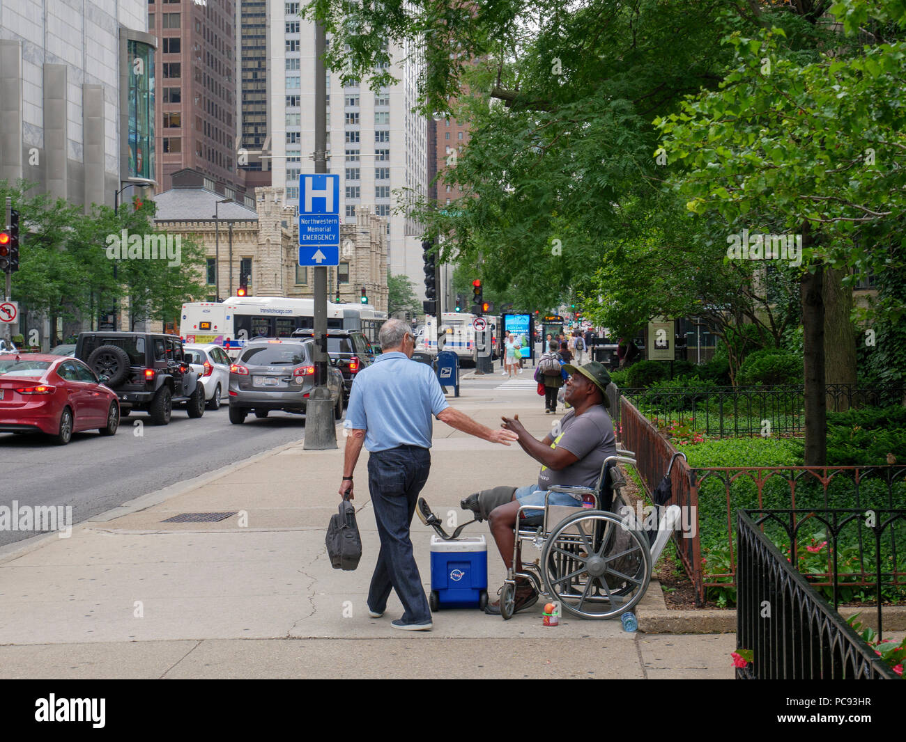 Disabled homeless man in wheelchair greeted by man walking by Stock