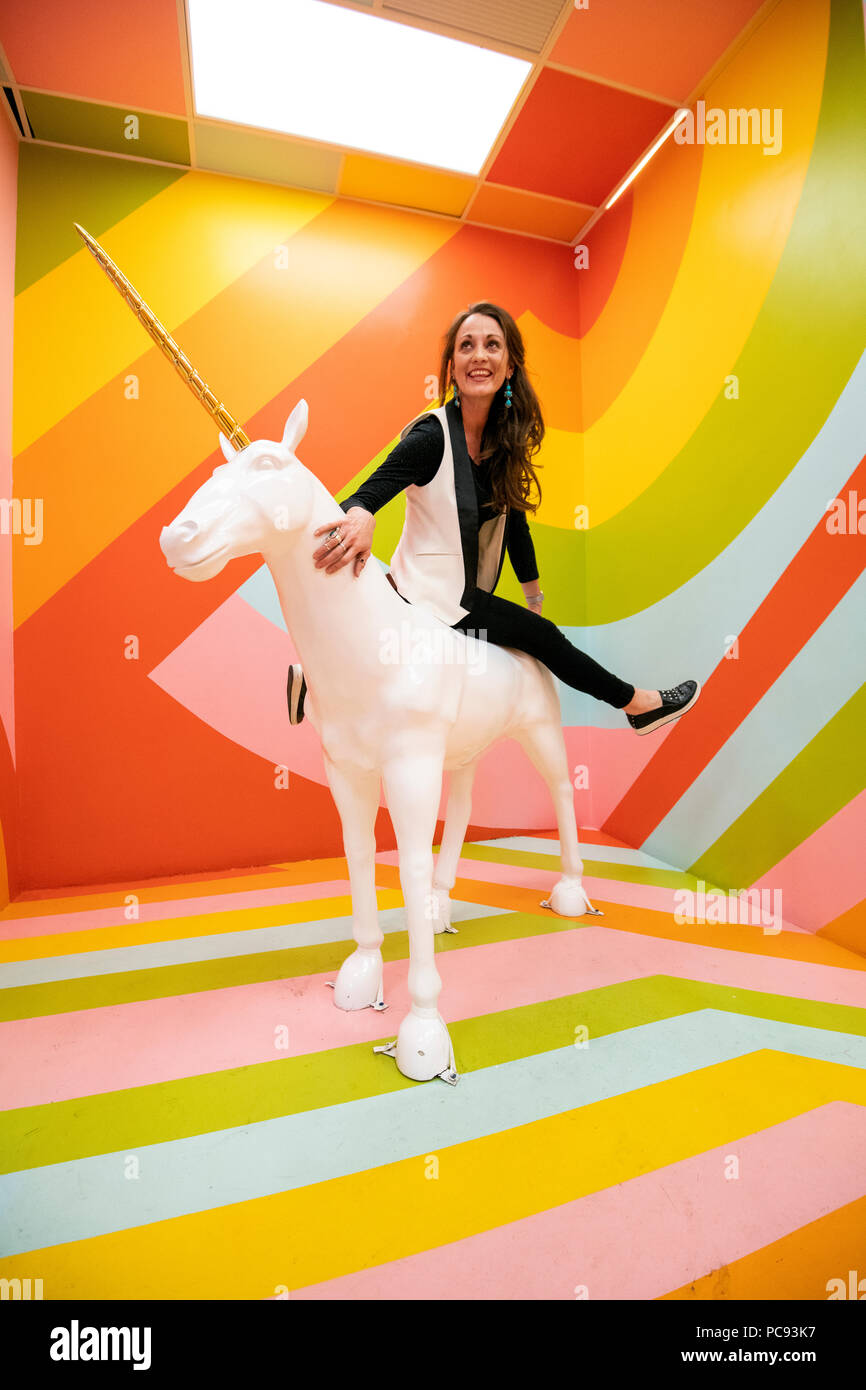 A woman rides a unicorn in a multicolored room at the Museum of Ice Cream in San Francisco, California. Stock Photo