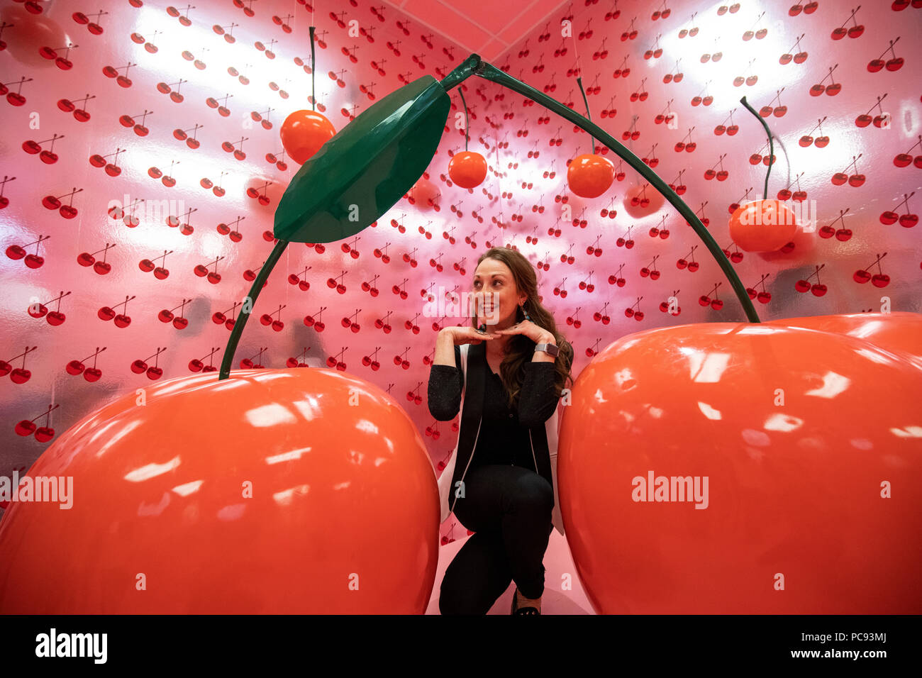 A woman kneels by two large cherries at the Museum of Ice Cream in San Francisco, California. Stock Photo