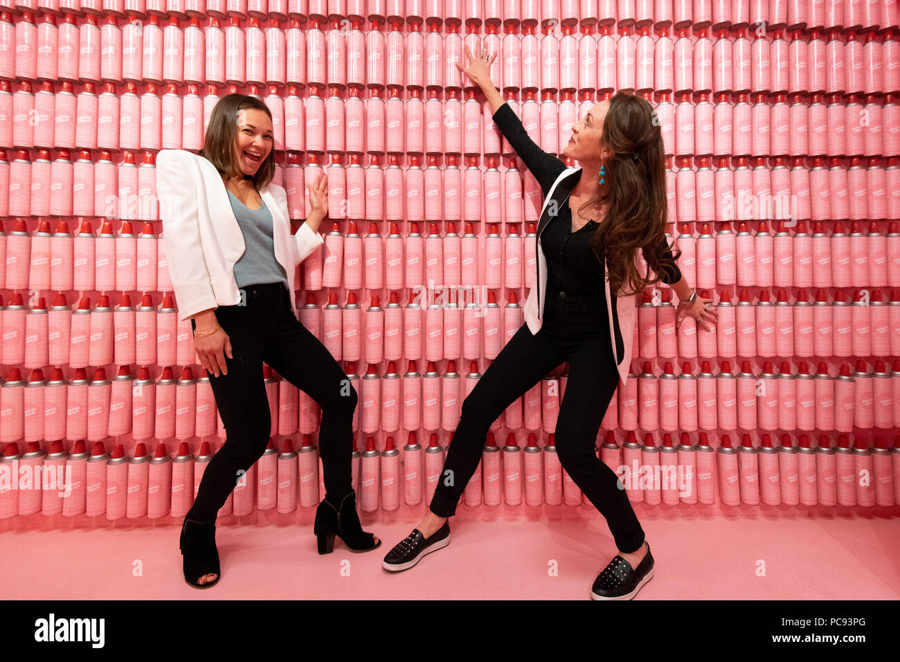 Two women stand by a pink wall of whipped cream cans in the Museum of Ice Cream in San Francisco, California. Stock Photo