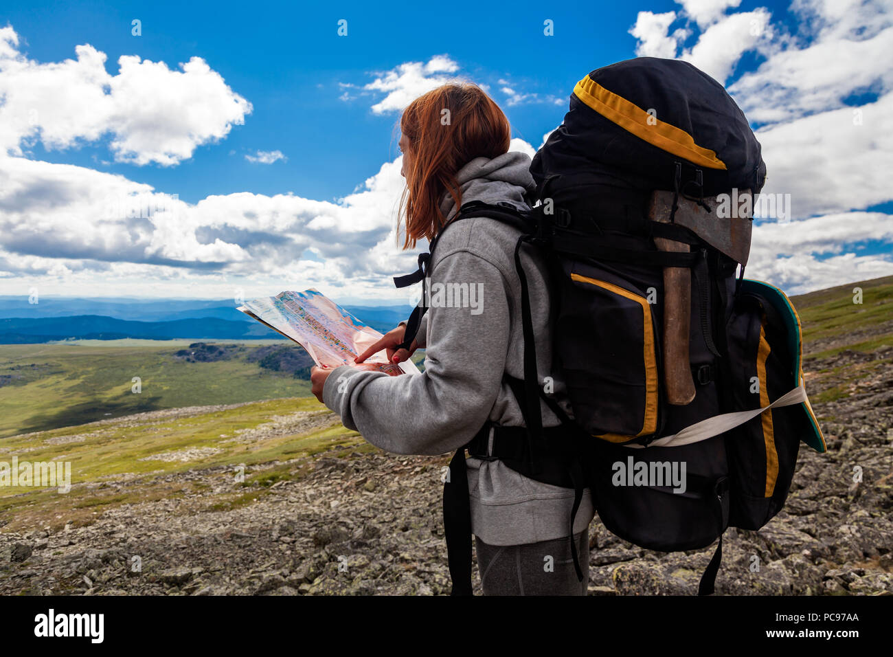 Stylish woman with backpack hiking, orient themselves to the terrain, study map and navigate the 