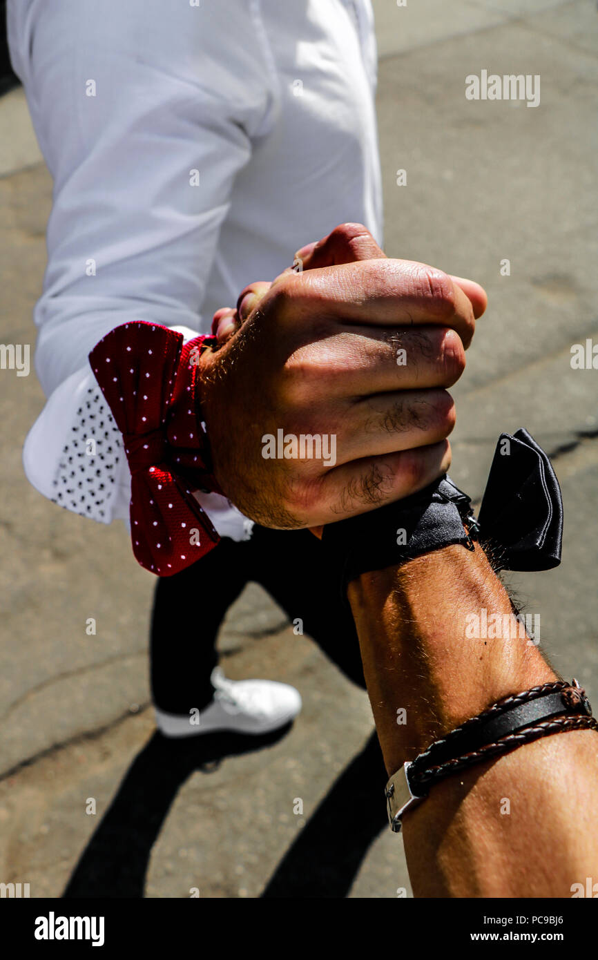 Best friends going to wedding, shaking hands, wearing polka dotted red bow tie and a blue tie, brown bracelet and a white shirt. Stock Photo