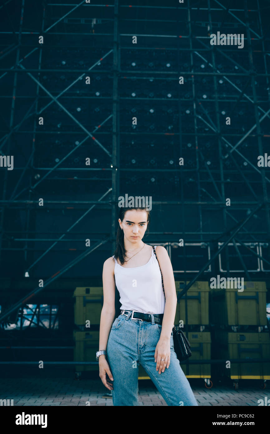 Beautiful young woman standing on the backstage of outdoor concert. Girl  dressed in jeans and white top posing in the city Stock Photo - Alamy