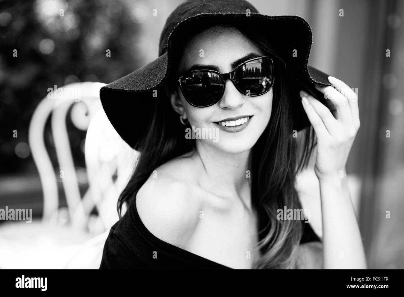 Young pretty girl in a black hat sitting in a cafe on the street and drinking cooled beverage Stock Photo
