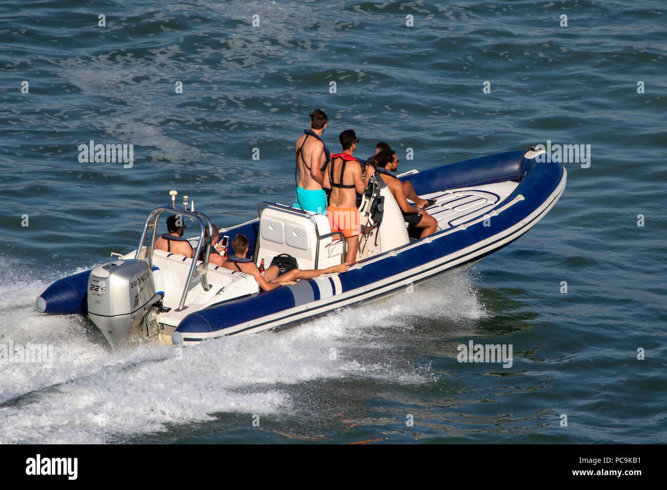 Group of young men riding an inflatable rib dinghy boat on the Solent in Southampton Stock Photo