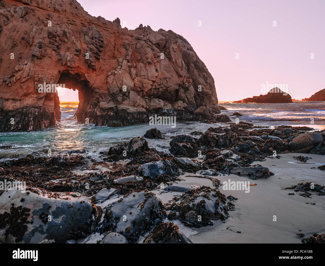 Panoramic view of the Keyhole Arch cliff at Pfeiffer Big Sur State Park beach in California. Black rocks in the foreground. Light of the setting sun. Stock Photo