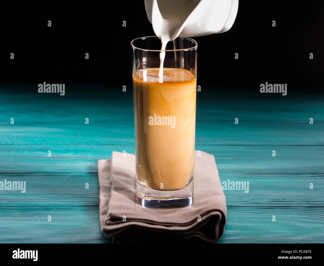 Glass of iced coffee on dark background. Pouring milk cream in motion