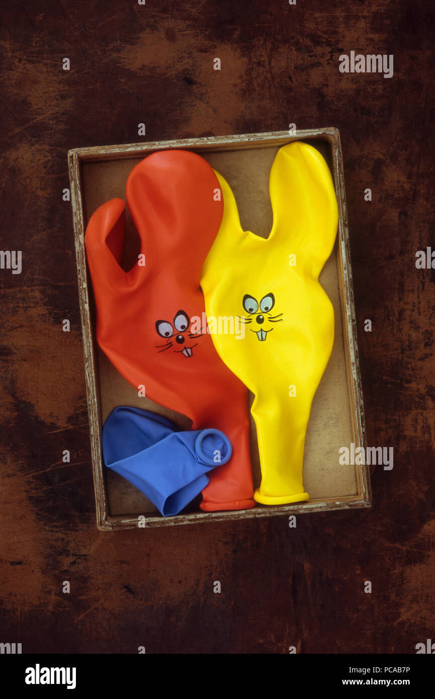 Three deflated party balloons with rabbit ears and faces lying in cardboard box Stock Photo