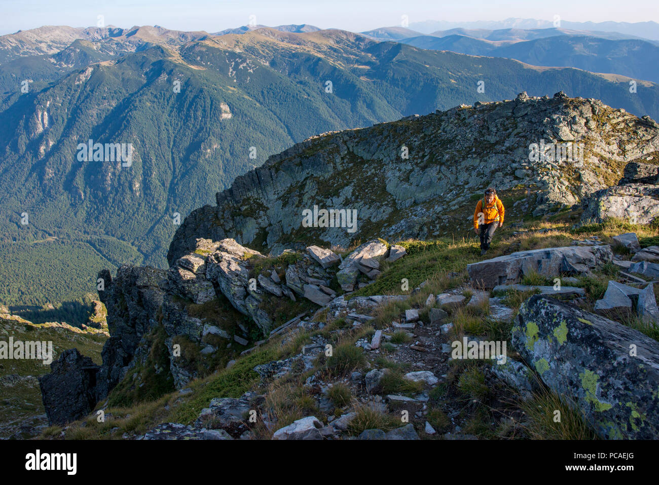 A hiker climbs along a high ridge near Maliovitsa in the Rila Mountains with distant views of valleys and hills, Bulgaria, Europe Stock Photo