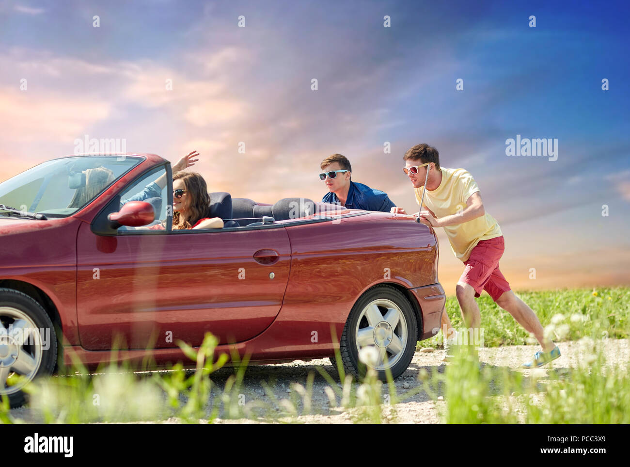 friends pushing broken convertible car Stock Photo