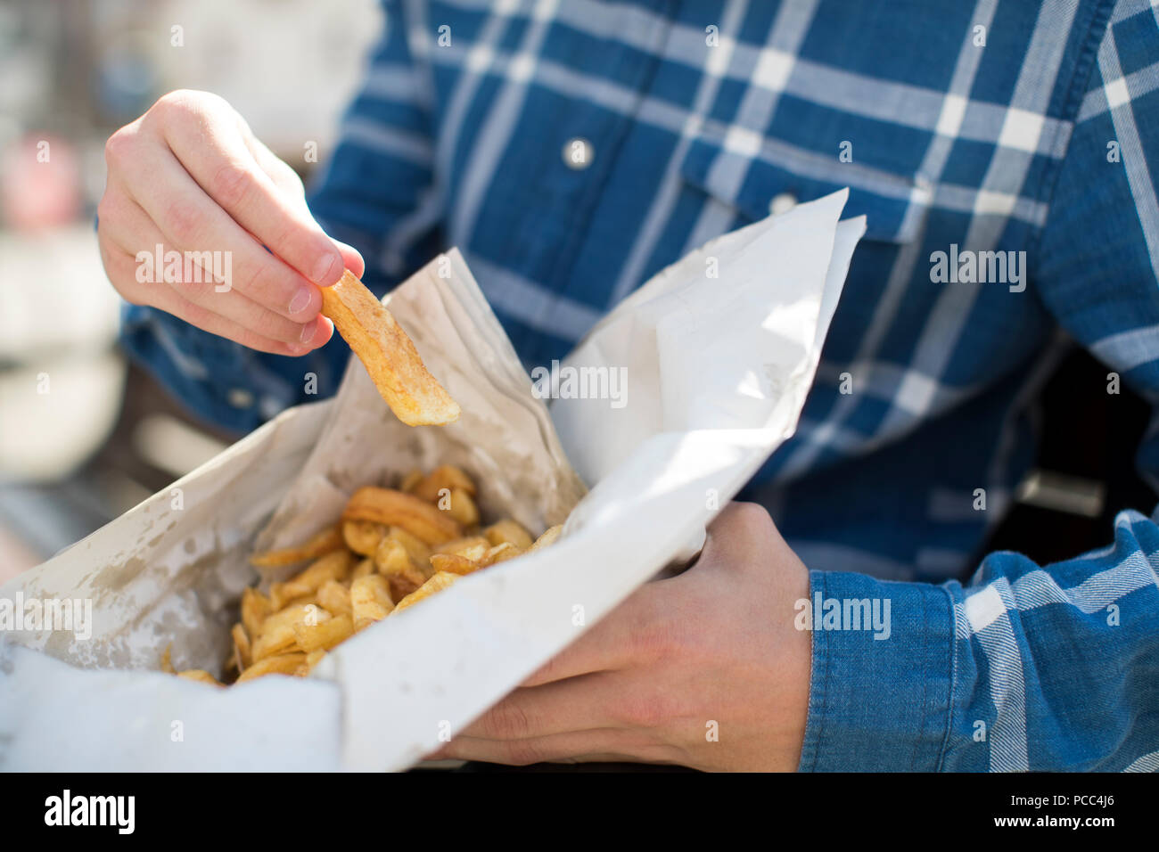 Close Up Of Teenage Boy Eating French Fries Sitting On Bench Outdoors Stock Photo