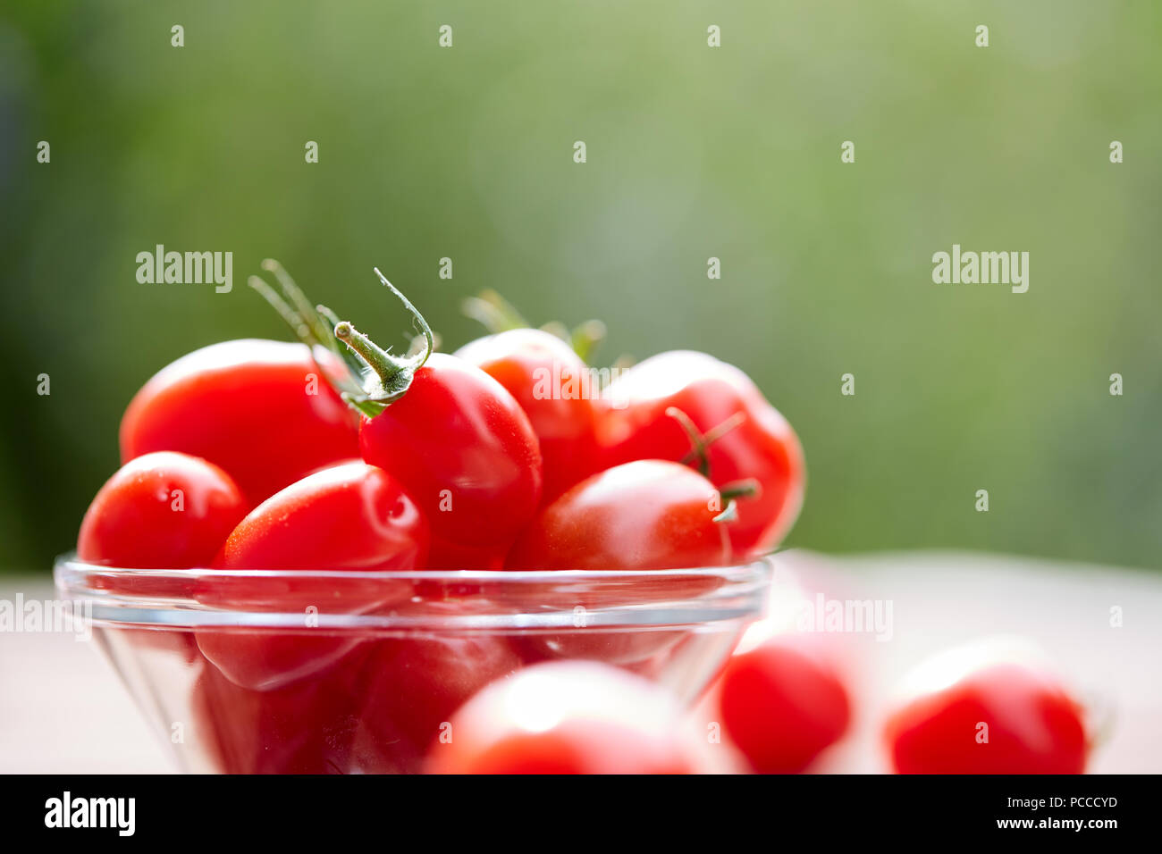 Tomatoes in a glass bowl on a wooden table Stock Photo - Alamy