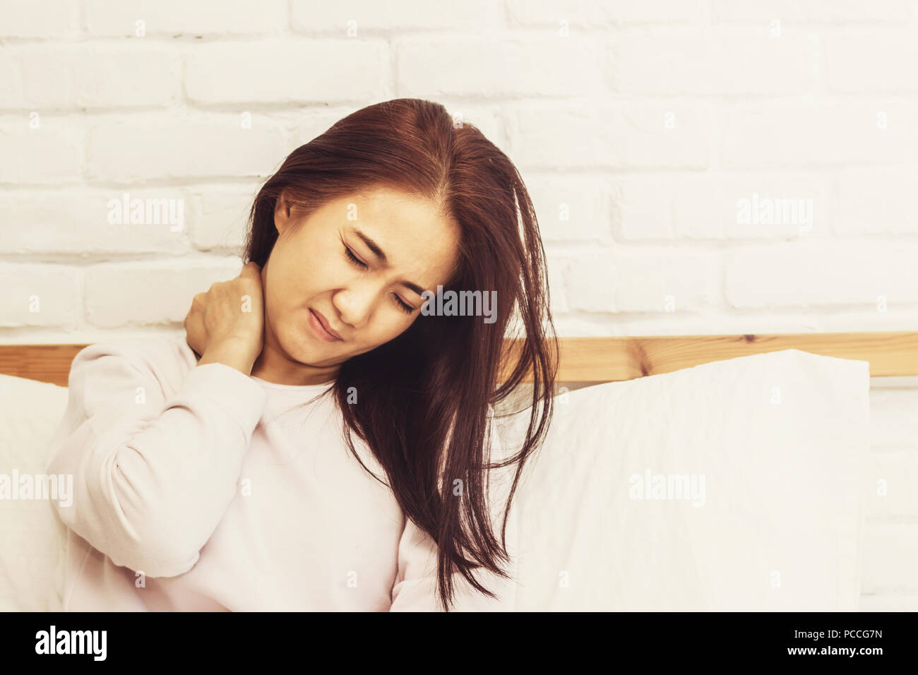 Asian woman back pain and sit on bed in bedroom in the morning Stock