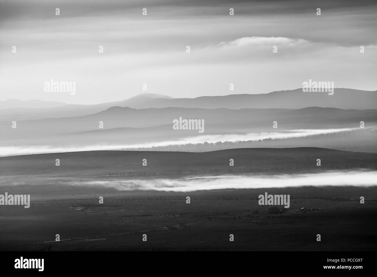 Layers of rugged mountains with patches of low clouds in the morning in black and white Stock Photo