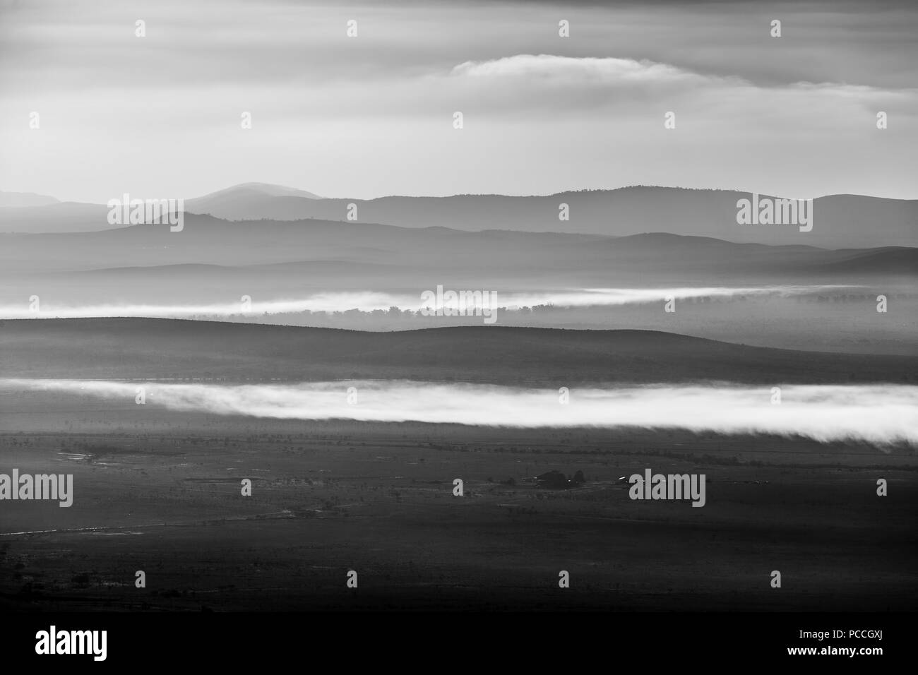 Black and white landscape of clouds low above land and mountains at sunrise Stock Photo