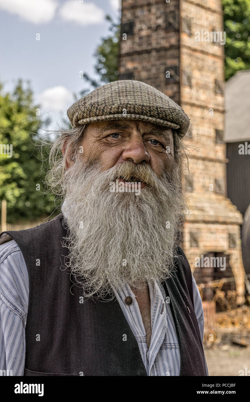 Portrait, front view close up of old traditional UK canal boat man in tweed flat cap with long grey beard, isolated outdoors, Black Country Museum, UK. Stock Photo