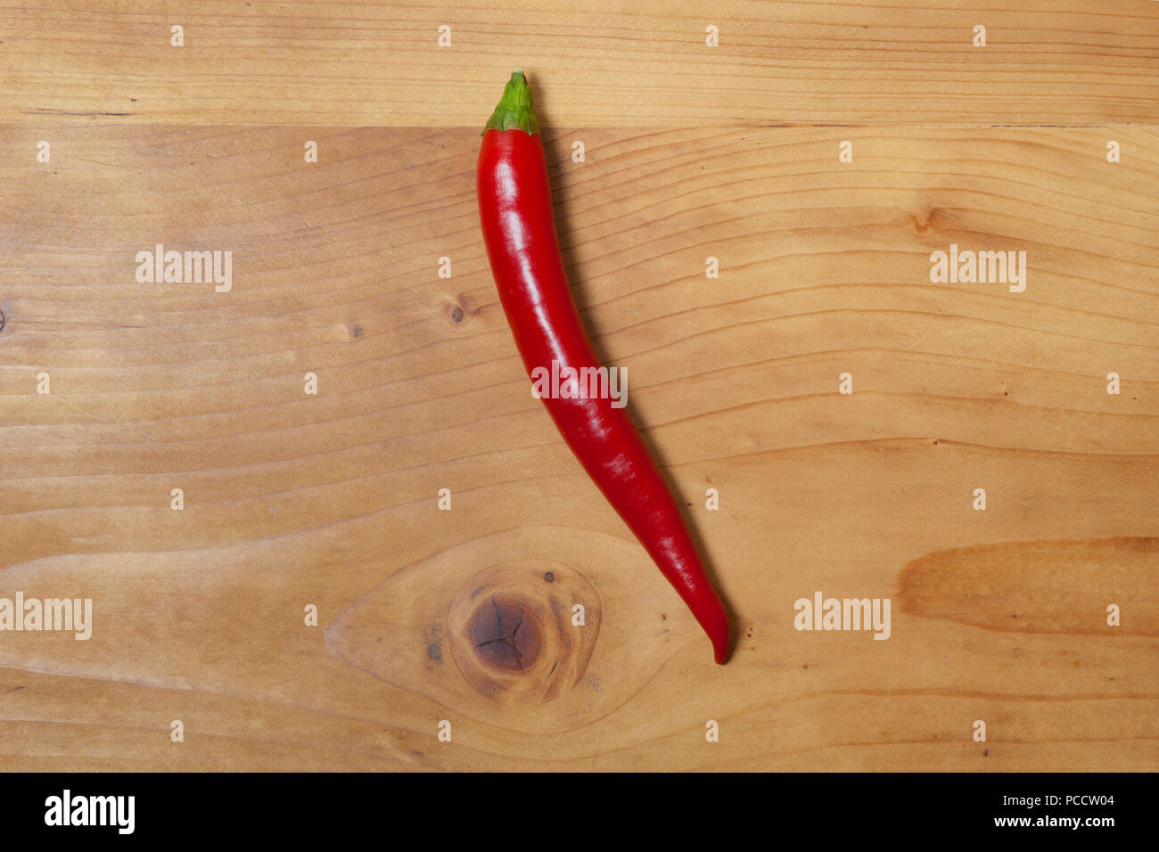 Isolated single red hot chilli pepper for ingredient of spicy meal or salad on natural wooden table top from above Stock Photo