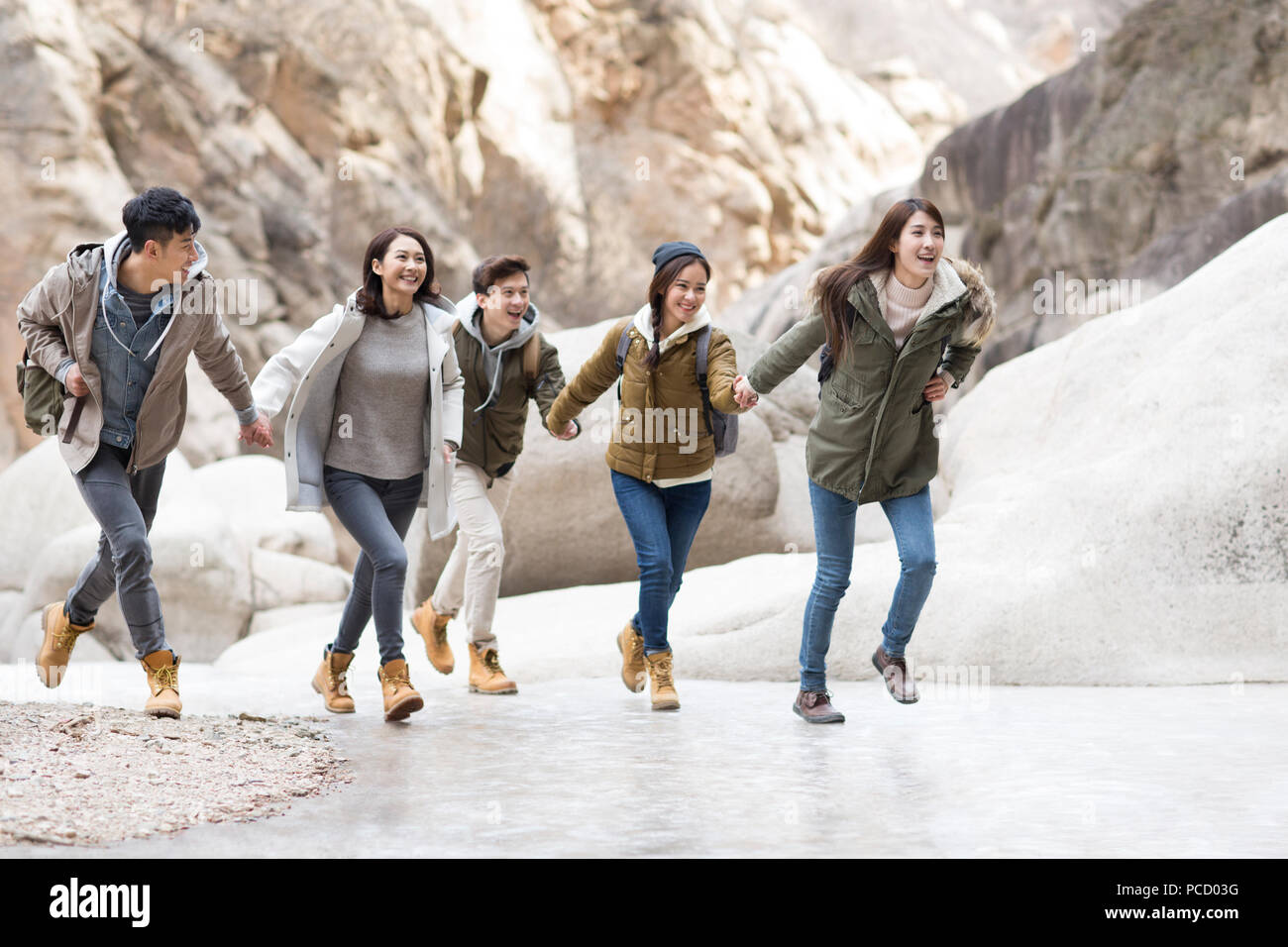 Happy young Chinese friends holding hands running outdoors in winter Stock Photo