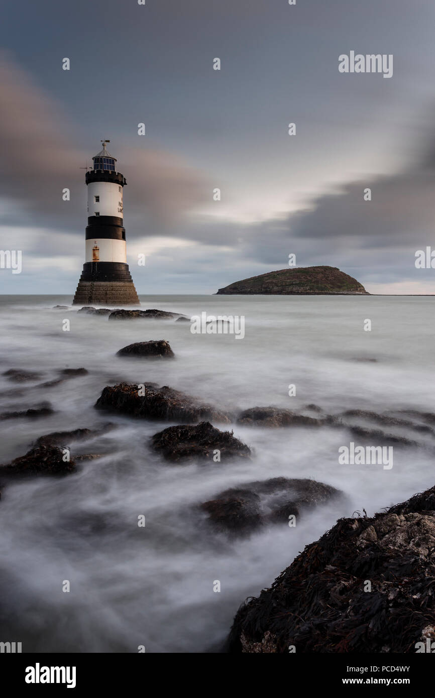 Lighthouse at Penmon Point, Anglesey, North Wales with a rocky shoreline Stock Photo