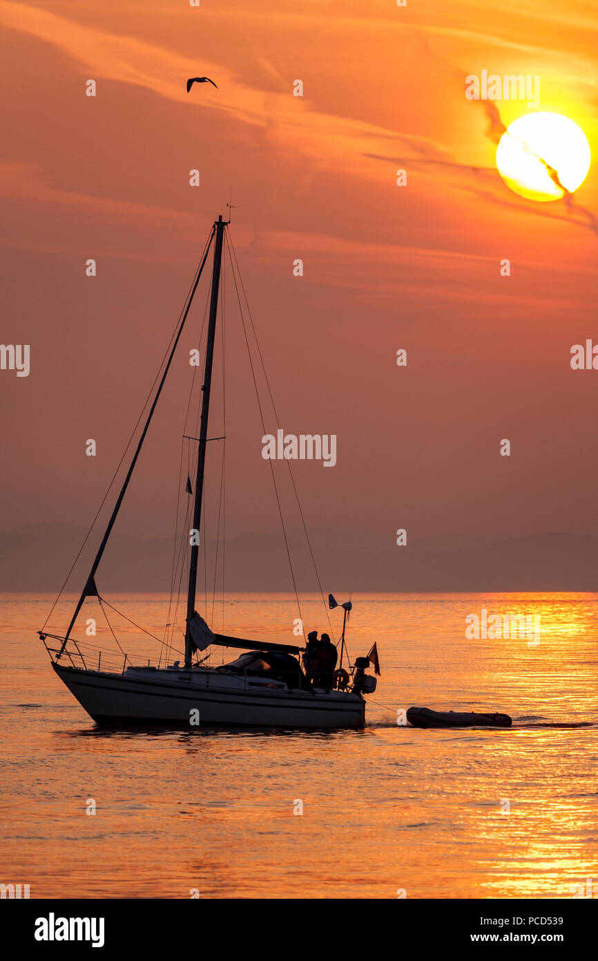 Yacht sailing on a calm sea at sunrise off Penmon Point, Anglesey, North Wales Stock Photo