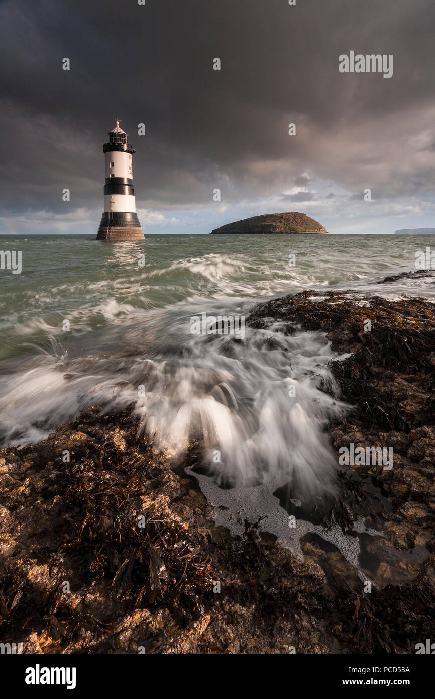 Lighthouse at Penmon Point under clouds, Anglesey, North Wales with Puffin Island in the background Stock Photo