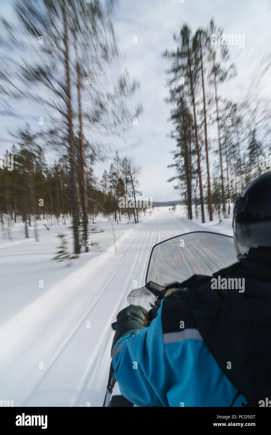 Senior woman traveler on snowmobile, speeding through the blurred trees, Torassieppi, Lapland, Northern Finland, Europe Stock Photo