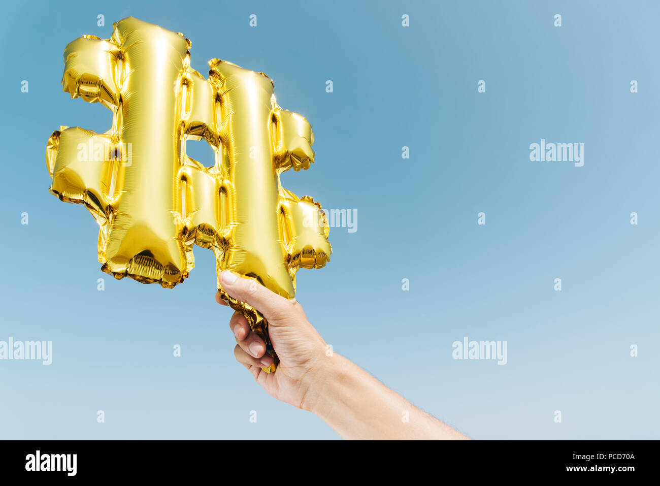 closeup of the hands of a young caucasian man on the beach holding a balloon in the shape of a hash symbol against the sky, with some blank space Stock Photo