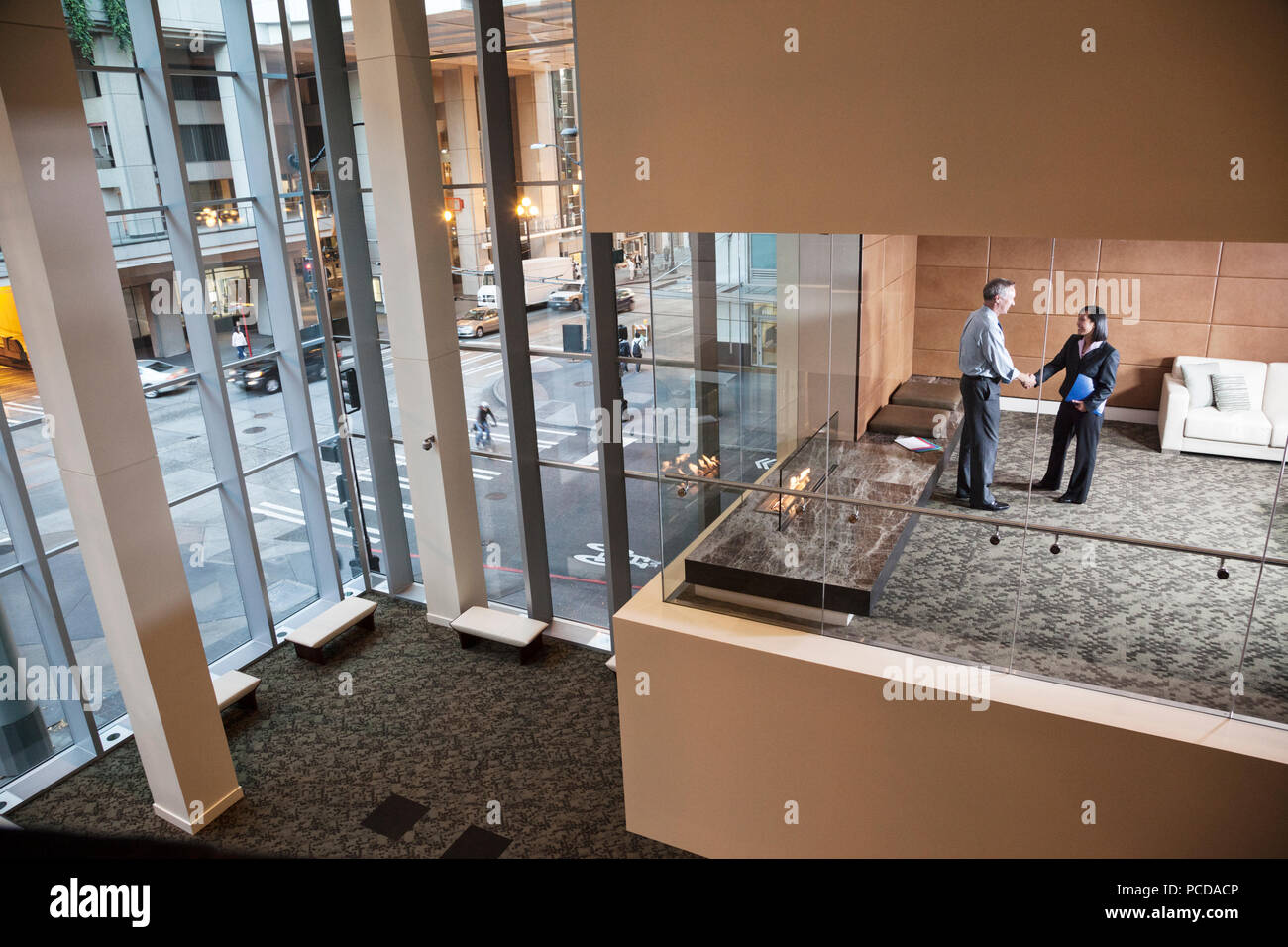 A large building, lobby, view looking into an office with glass walls, two business people talking. Stock Photo